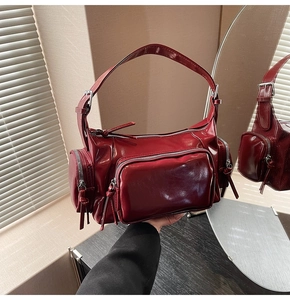Detail view of burgundy patent leather bag showing multiple zipped pockets and glossy finish
