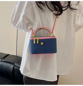 Detail of a denim box crossbody bag with pink trim and gold metal handle on a person