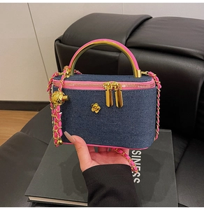 Detail of denim box bag featuring gold camellia logo and pink leather chain strap