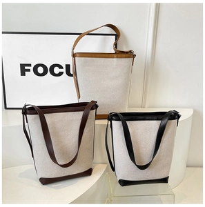 Three minimalist canvas and leather bucket bags in camel, coffee and black on display
