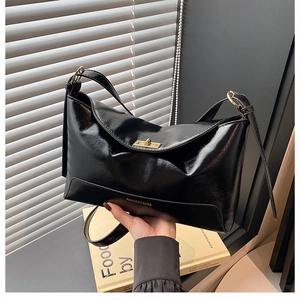 Detail of a black glossy tote bag with a golden twist lock and adjustable shoulder strap