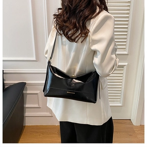 Close-up of black glossy leather tote bag with gold lettering shown on a white blazer