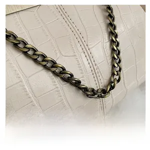Close-up of beige crocodile embossed leather and vintage bronze chain on shell bag