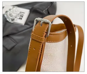 Detail of silver buckle and brown leather strap on cream canvas bucket bag
