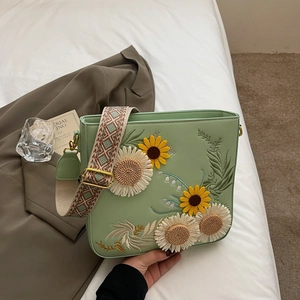 Light green shoulder bag with floral embroidery and wide woven strap on blazer background