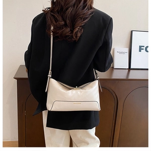 Detail of a minimalist cream shoulder bag with adjustable strap and gold brand lettering