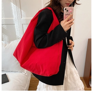 Close-up of a large red canvas tote bag worn by a model in casual professional attire