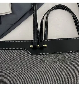 Macro view of grey woven canvas tote bag with black leather trim and gold hardware