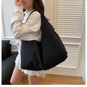 Model showing large black nylon tote bag in a minimalist indoor setting for daily use