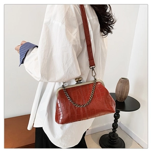 Detail of brick red crocodile embossed evening bag with retro metal kiss-lock and gold chain