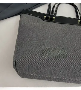 Detail of grey denim tote bag showing fabric texture and black leather stitching finish