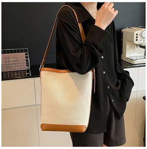 Detail of canvas bucket bag with brown leather trim carried by a model in a modern home