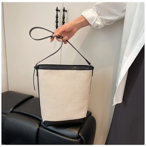 Detail of cream canvas bucket bag with black leather trim held by hand in a home setting