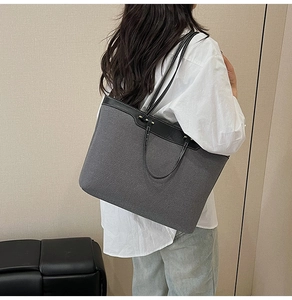 Detail of grey denim tote bag with black leather straps on a model in white shirt