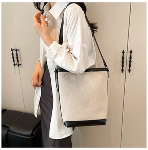 Detailed view of large canvas bucket bag with black leather trim worn on the shoulder