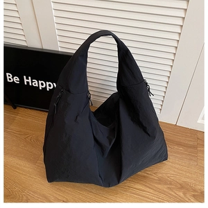 Detail of black nylon hobo tote featuring zipper accents and soft texture on wooden floor