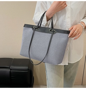 Detailed view of large tote bag with blue denim texture and black leather stitching detail