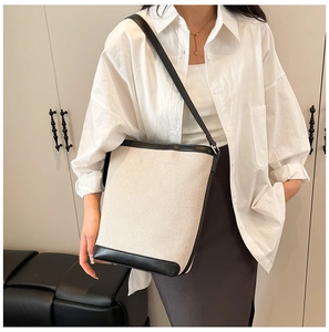 Detail of minimalist bucket bag featuring cream canvas and black leather patchwork