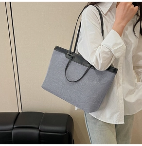Detail of large denim tote bag featuring black leather trim and twin shoulder straps