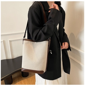 Side view of beige canvas bucket bag with brown leather trim worn by model in room
