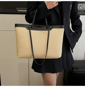 Large beige canvas tote bag with black leather straps styled with a black blazer