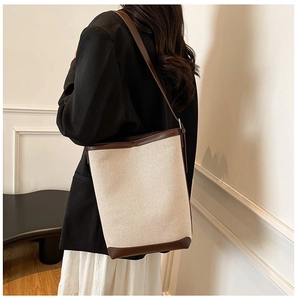 Model wearing a two-tone bucket bag featuring cream canvas and dark brown leather trim