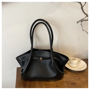 Detailansicht der schwarzen Plissee-Ledertasche mit goldener Schnalle auf Holztisch