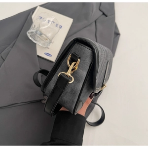 Detail of dark gray denim crossbody bag with black leather trim and gold metal hooks