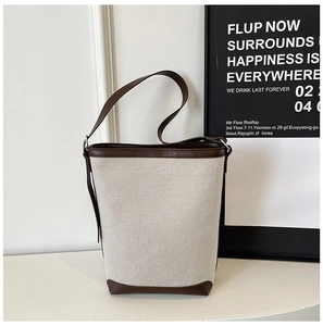 Detail of canvas bucket bag with brown leather trim and stitching on textured fabric