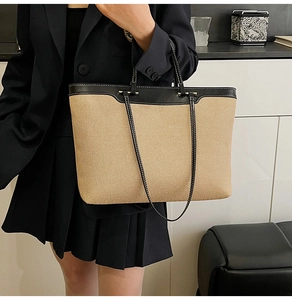 Macro detail of beige woven canvas tote bag with black leather trim and handle finish
