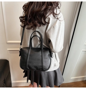 Detail of black lychee grain leather handbag shown on model in stylish indoor setting