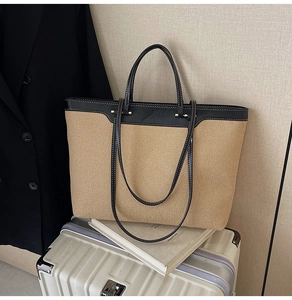 Detail of khaki woven tote bag with black leather handles on a white suitcase
