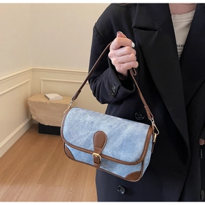 Close-up of light blue denim shoulder bag with brown leather trim and golden buckle
