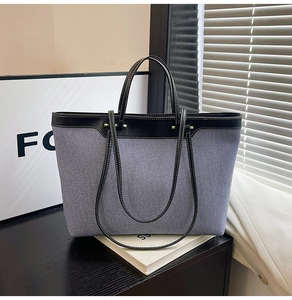 Detail of gray-blue canvas tote with black leather straps and gold metal hardware