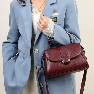 Détail d'un sac en cuir vintage bordeaux avec fermoir rotatif porté par un mannequin