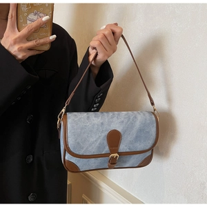 Detail of light blue denim shoulder bag with brown leather trim held by a model