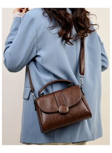 Détail d'un sac à main vintage marron foncé avec boucle ronde sur un blazer bleu clair