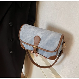 Detail of blue denim shoulder bag featuring brown leather trim and metal buckle closure