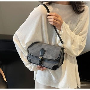 Close-up of retro denim shoulder bag with black leather trim worn on a white top