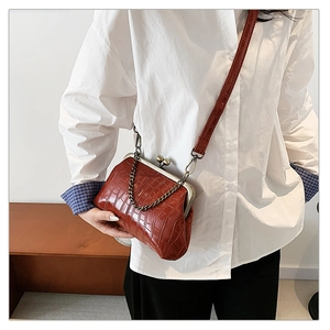 Detail of reddish-brown crocodile embossed handbag with vintage metal clasp and chain strap