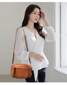 Brown lychee leather crossbody camera bag with metal rivet details worn by a model