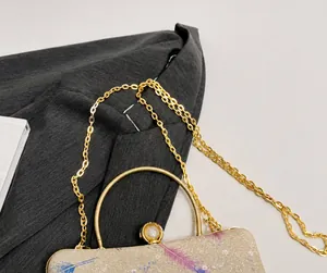 Detalle del asa de metal dorado y la cadena fina en el bolso de lentejuelas con plumas