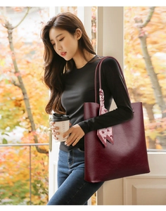 Detail shot of a burgundy leather tote bag with a decorative heart pattern silk scarf handle