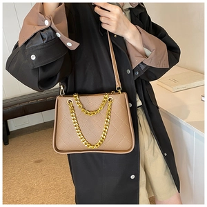 Détail d'un sac bandoulière marron matelassé avec une chaîne dorée et cuir souple