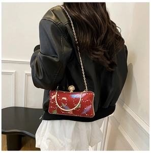 Detalle de bolso de noche rojo con lentejuelas, estampado de plumas y cierre de perla