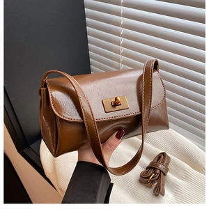 Detail of dark brown leather handbag featuring a golden turn-lock closure and adjustable strap