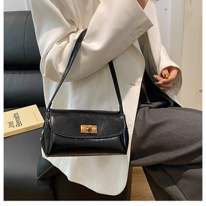 Detail shot of a black glossy vintage square bag with gold metal lock on a model