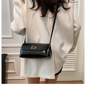 Detail of vintage black leather crossbody bag with gold metal clasp on white suit
