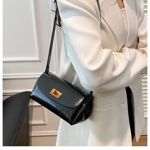 Detail of glossy black crossbody bag featuring a classic golden rotating lock on the front