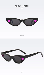 Detail view of black cat-eye sunglasses featuring pink heart accents and grey lenses